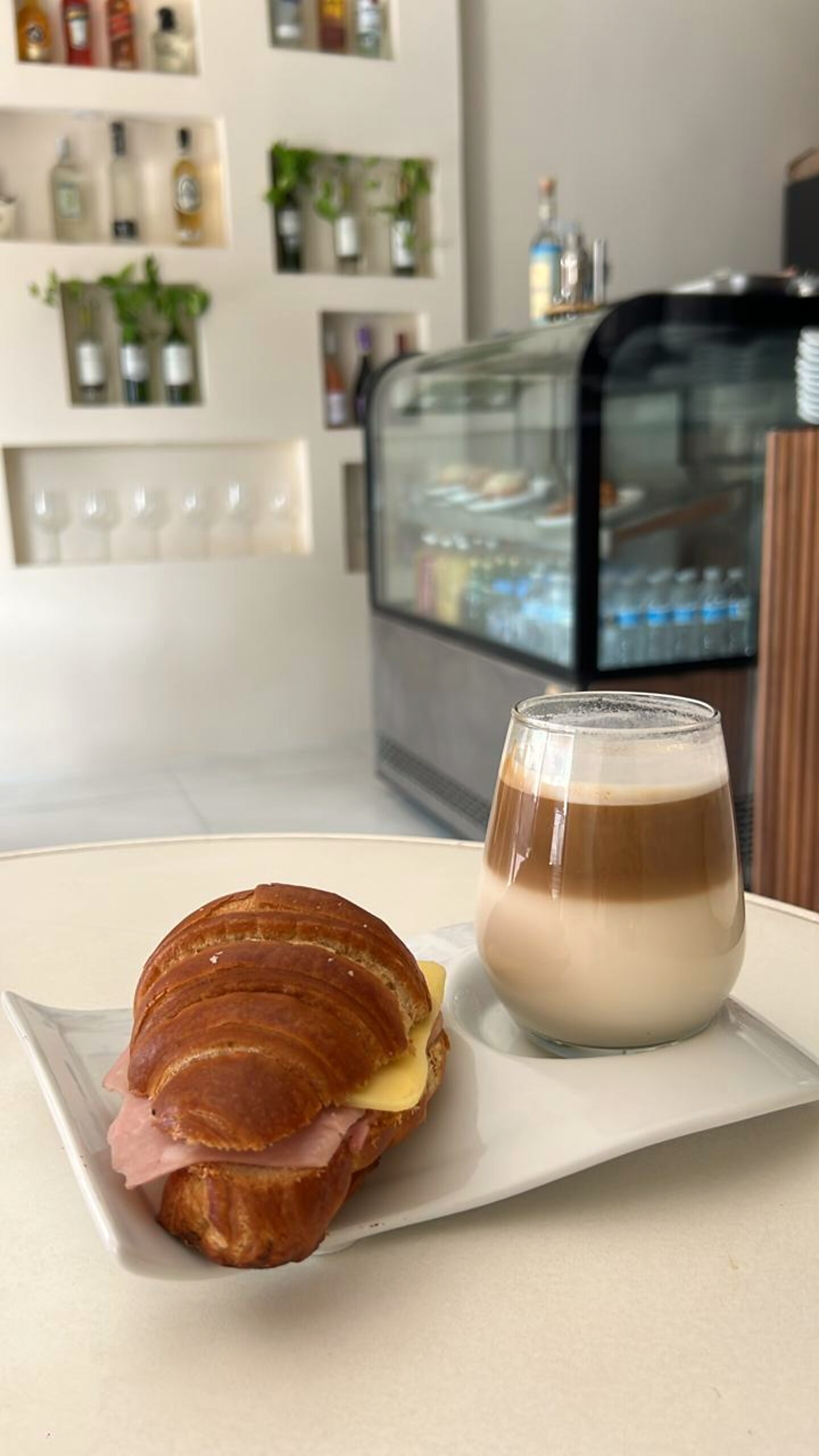 Capuchino en vaso de vidrio con croissant de jamón y queso