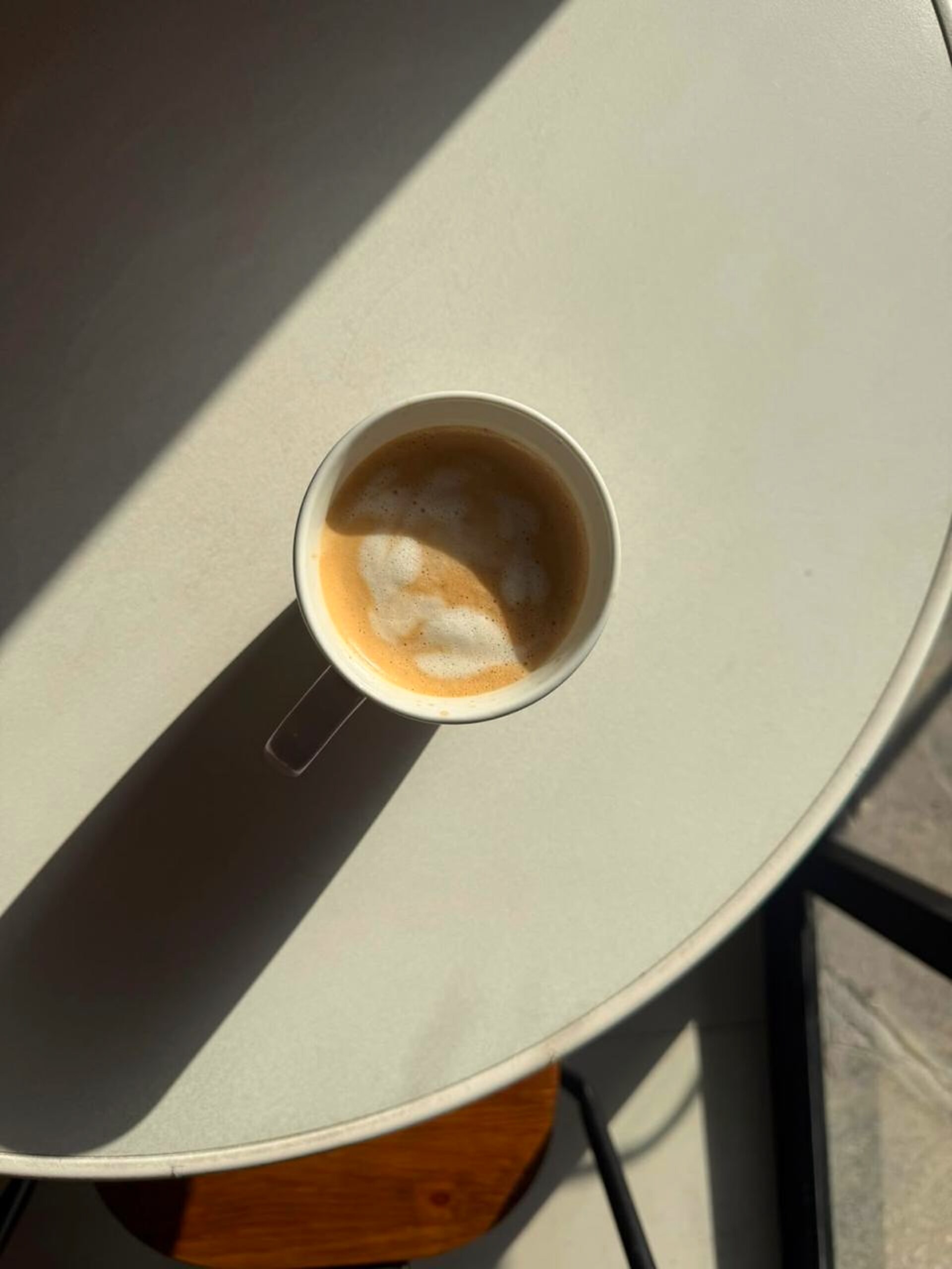 Taza de café con espuma sobre mesa iluminada por el sol