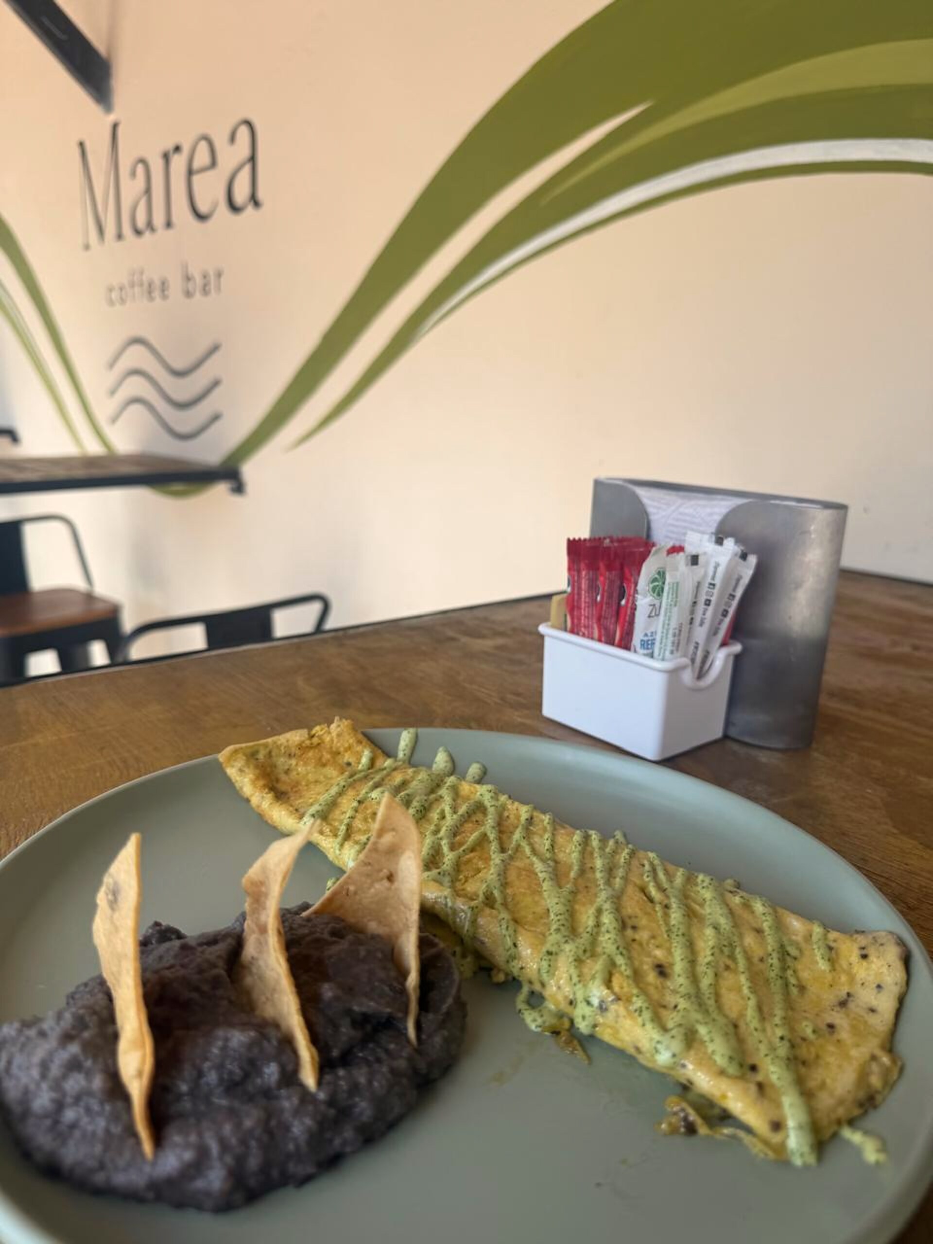 Omelette con salsa verde y frijoles frente al mural del logo